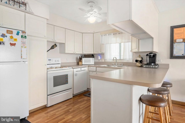 kitchen featuring white appliances, a peninsula, a sink, white cabinets, and light wood-type flooring