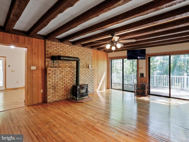 unfurnished living room featuring light hardwood / wood-style flooring, ceiling fan, beam ceiling, wooden walls, and a wood stove