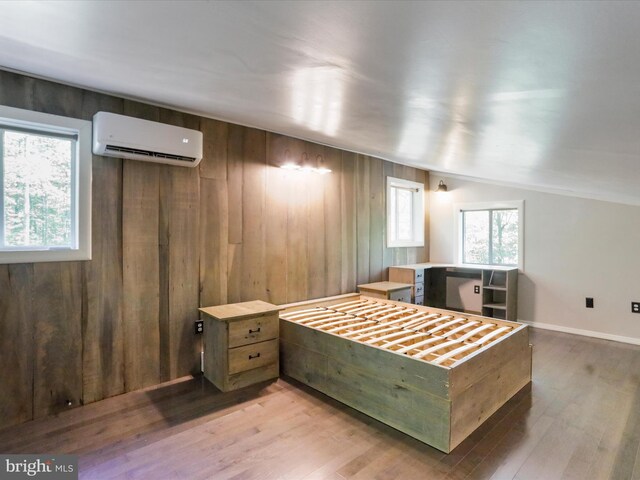 bedroom with lofted ceiling, a wall unit AC, and light hardwood / wood-style flooring