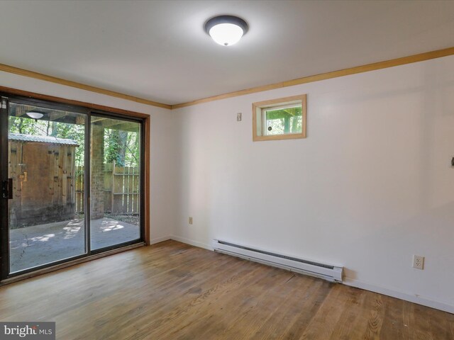 empty room with wood-type flooring, a baseboard heating unit, and crown molding