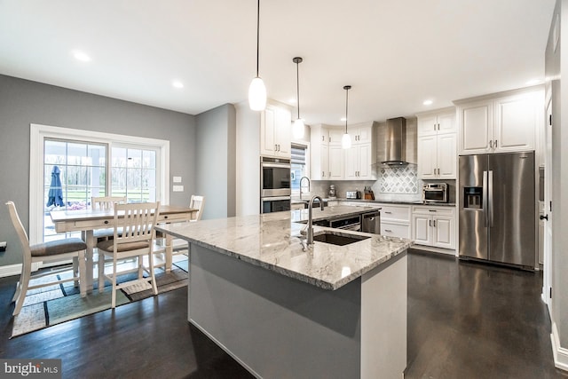 kitchen with appliances with stainless steel finishes, hanging light fixtures, dark hardwood / wood-style floors, tasteful backsplash, and wall chimney range hood