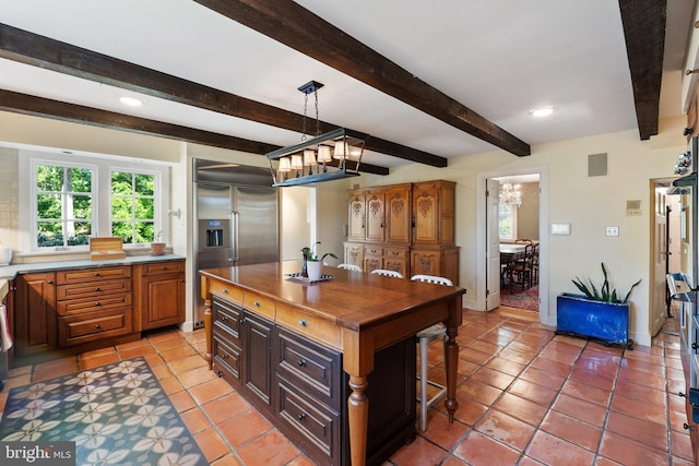 kitchen with a kitchen bar, wood counters, beamed ceiling, a center island, and built in refrigerator