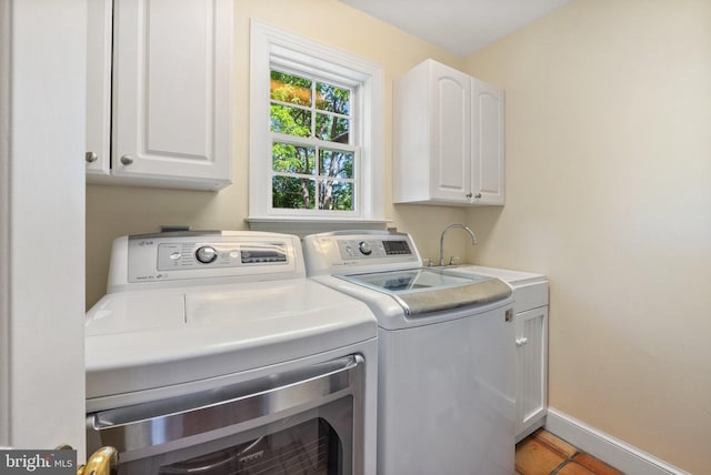 clothes washing area featuring washer and clothes dryer, light tile patterned flooring, and cabinets