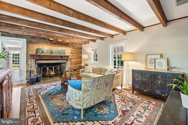 living room with beam ceiling, hardwood / wood-style flooring, and a stone fireplace