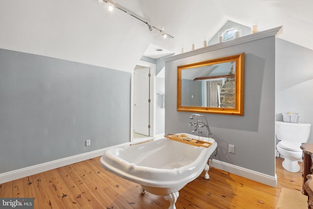 bathroom featuring lofted ceiling, rail lighting, a washtub, toilet, and wood-type flooring