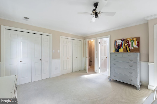 unfurnished bedroom featuring ceiling fan, crown molding, light carpet, and two closets