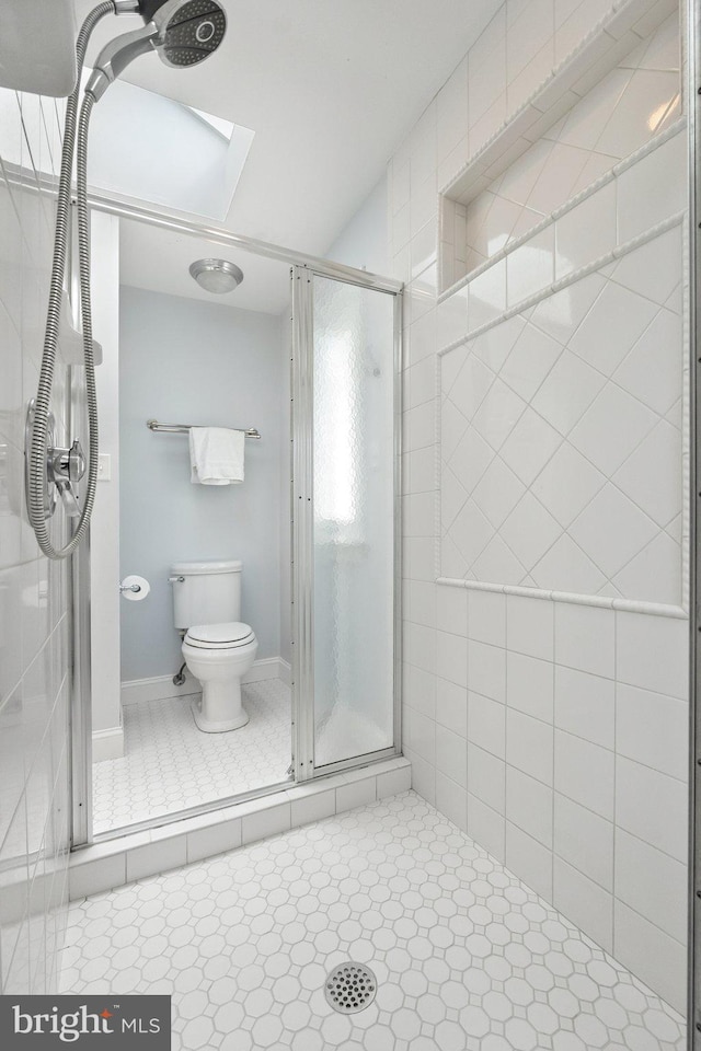 bathroom featuring a skylight, toilet, a shower with door, and tile patterned flooring