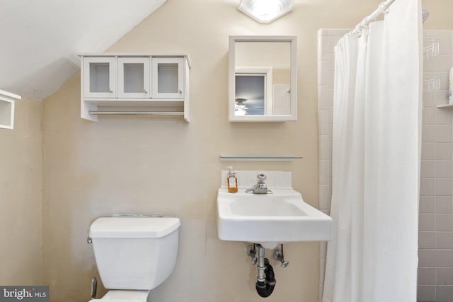 bathroom featuring curtained shower, sink, lofted ceiling, and toilet