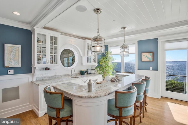 kitchen with a water view, decorative light fixtures, light stone countertops, and white cabinetry