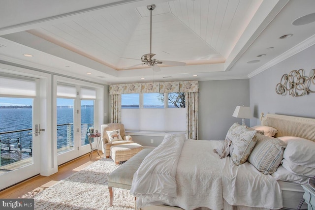 bedroom with multiple windows, a raised ceiling, access to outside, and a water view