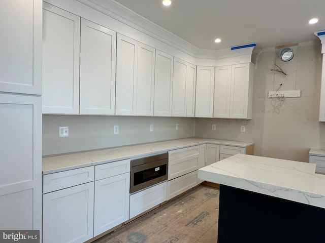 kitchen featuring light stone countertops, white cabinetry, stainless steel microwave, and ornamental molding