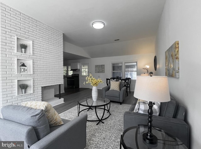 living room featuring lofted ceiling, brick wall, and hardwood / wood-style flooring