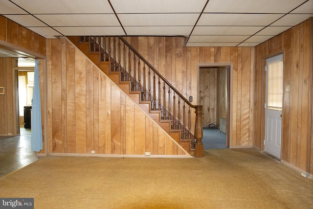 interior space featuring a paneled ceiling, wooden walls, and carpet floors