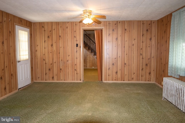 carpeted spare room with radiator, wood walls, and ceiling fan