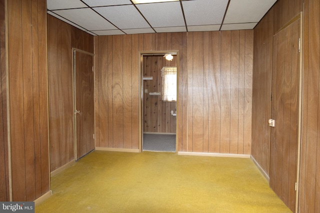 carpeted empty room with a paneled ceiling and wooden walls