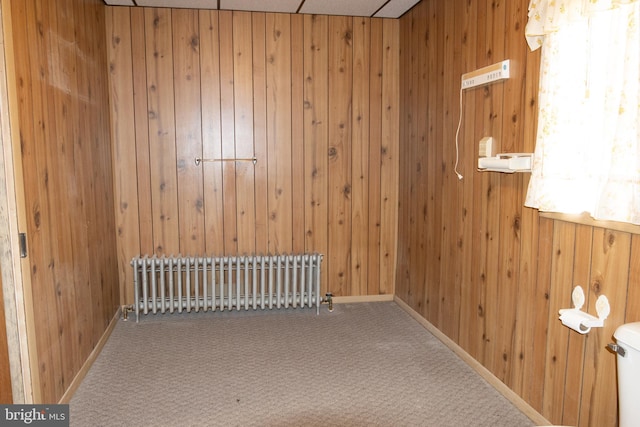 spare room featuring carpet flooring, wood walls, and radiator