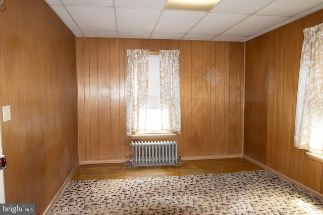 empty room with a paneled ceiling, radiator, and wood walls