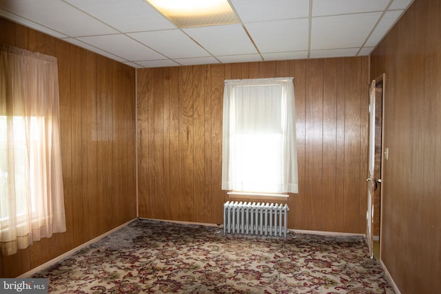 empty room with a drop ceiling, wood walls, and radiator heating unit