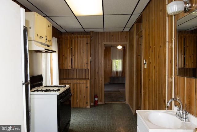 kitchen featuring wooden walls, radiator heating unit, white appliances, and sink