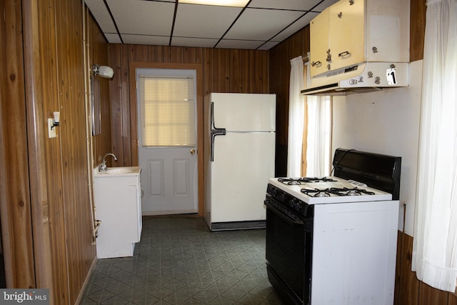 kitchen with a drop ceiling, white appliances, sink, and wooden walls