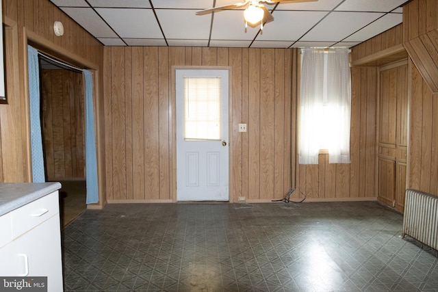 foyer entrance featuring ceiling fan, a drop ceiling, wood walls, and radiator