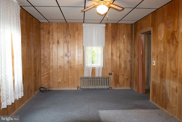 carpeted spare room featuring radiator heating unit, a paneled ceiling, ceiling fan, and wood walls