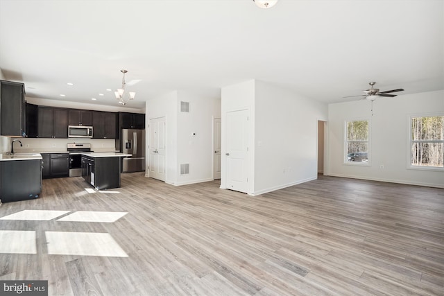 kitchen featuring light wood-type flooring, ceiling fan with notable chandelier, stainless steel appliances, sink, and a kitchen island