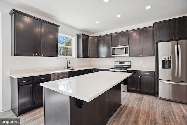 kitchen with dark brown cabinetry, appliances with stainless steel finishes, a kitchen island, sink, and light hardwood / wood-style flooring