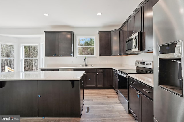 kitchen featuring sink, appliances with stainless steel finishes, light hardwood / wood-style floors, dark brown cabinetry, and a breakfast bar