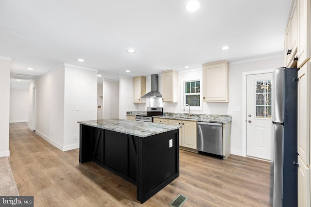 kitchen with wall chimney exhaust hood, light stone countertops, appliances with stainless steel finishes, sink, and light hardwood / wood-style floors