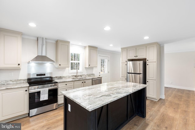 kitchen featuring light wood-type flooring, appliances with stainless steel finishes, wall chimney range hood, sink, and a kitchen island