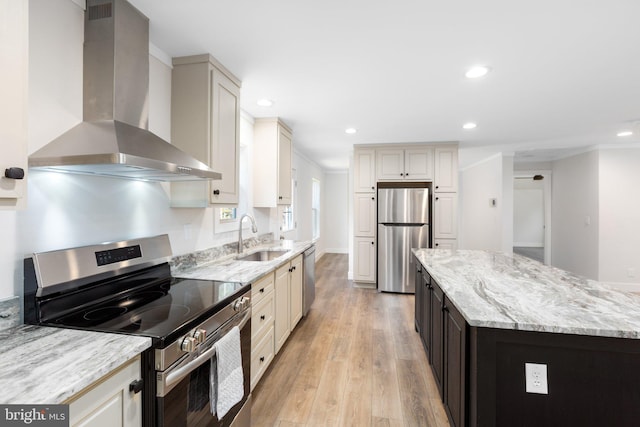 kitchen featuring light stone countertops, appliances with stainless steel finishes, wall chimney range hood, sink, and light wood-type flooring