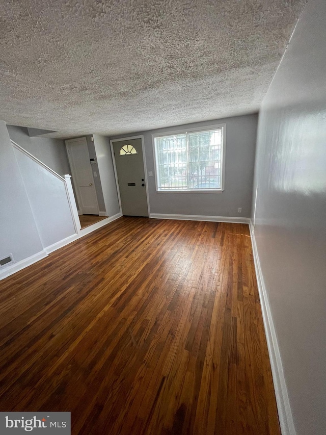 unfurnished living room with a textured ceiling and dark hardwood / wood-style floors