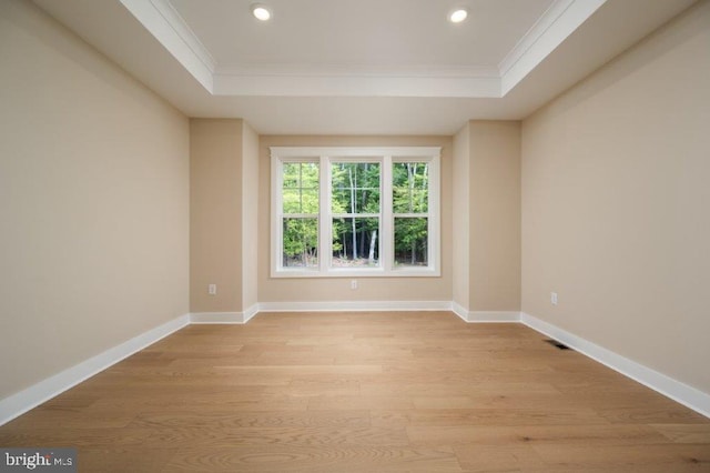 empty room featuring a tray ceiling, light wood-type flooring, and crown molding