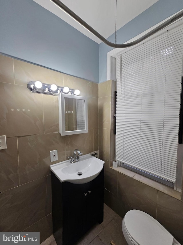 bathroom with toilet, vanity, tile patterned floors, and tile walls