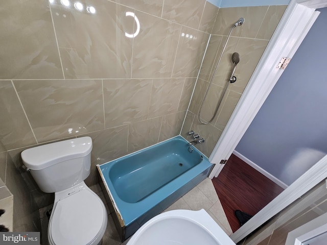 bathroom with toilet, tiled shower / bath, and tile walls