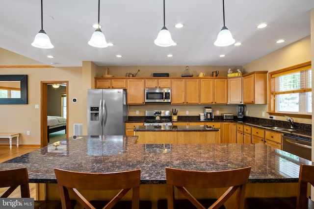 kitchen with appliances with stainless steel finishes, a center island, dark stone counters, hanging light fixtures, and hardwood / wood-style flooring