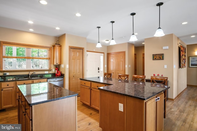 kitchen featuring a center island, dishwasher, light wood-type flooring, dark stone counters, and pendant lighting