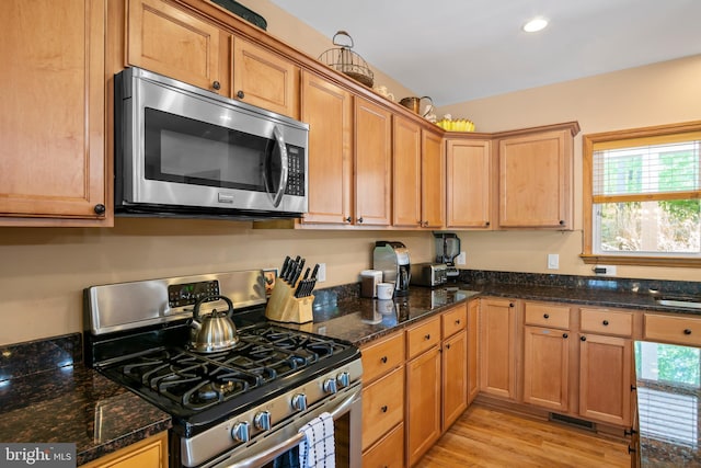 kitchen with plenty of natural light, light wood-type flooring, stainless steel appliances, and dark stone counters