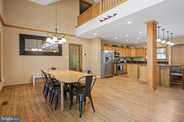 dining space with a notable chandelier, light hardwood / wood-style flooring, decorative columns, and a towering ceiling