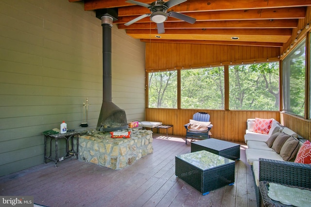 sunroom featuring a wood stove, lofted ceiling with beams, and ceiling fan