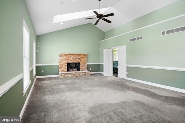 unfurnished living room with a skylight, ceiling fan, a fireplace, high vaulted ceiling, and dark colored carpet