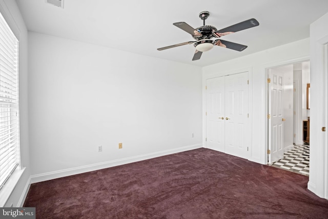 unfurnished bedroom with a closet, dark colored carpet, ceiling fan, and multiple windows