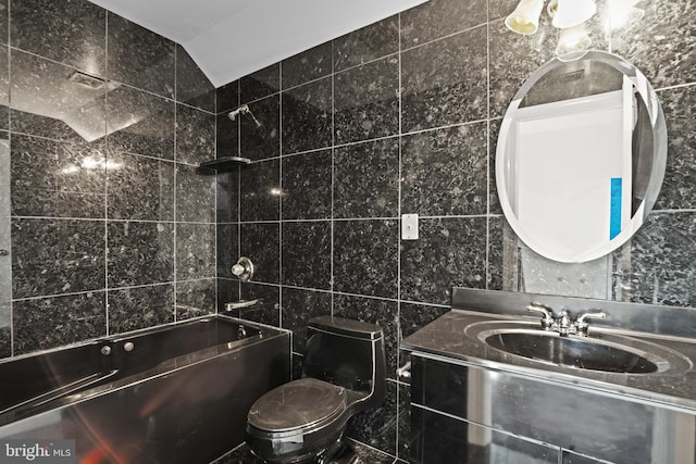 full bathroom with tiled shower / bath, toilet, tile walls, and vanity with extensive cabinet space