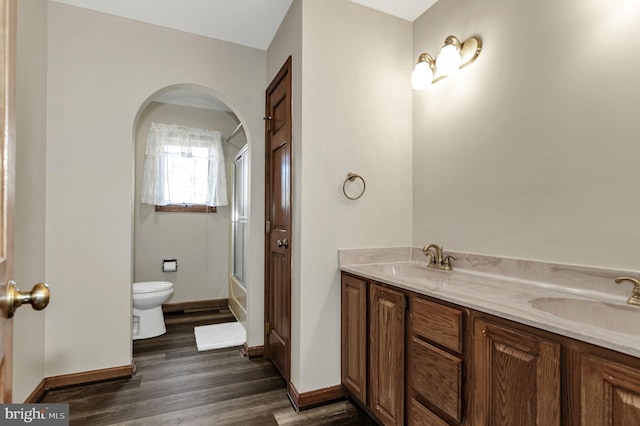 full bathroom with wood-type flooring, double vanity, bath / shower combo with glass door, and toilet