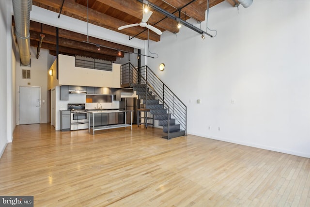 living room with sink, light hardwood / wood-style floors, a towering ceiling, and beamed ceiling