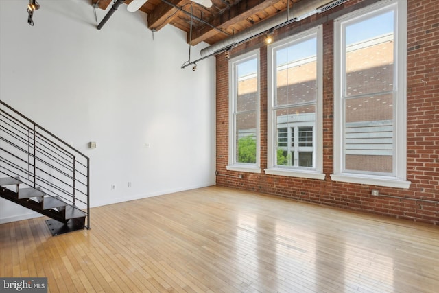 unfurnished living room featuring light hardwood / wood-style floors, a healthy amount of sunlight, beamed ceiling, and brick wall