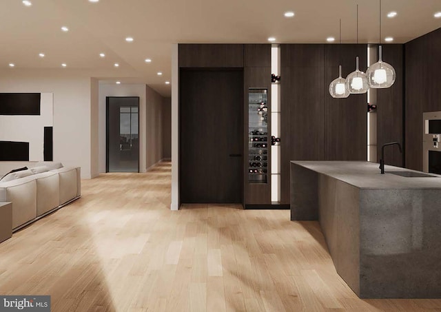 interior space with sink, wall oven, decorative light fixtures, dark brown cabinets, and light hardwood / wood-style flooring