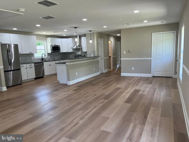 kitchen featuring wall chimney exhaust hood, stainless steel appliances, light hardwood / wood-style flooring, pendant lighting, and white cabinets