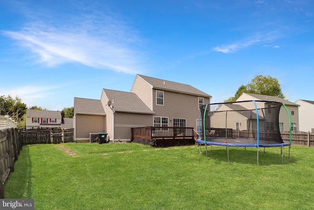 rear view of property featuring a trampoline, a deck, and a yard